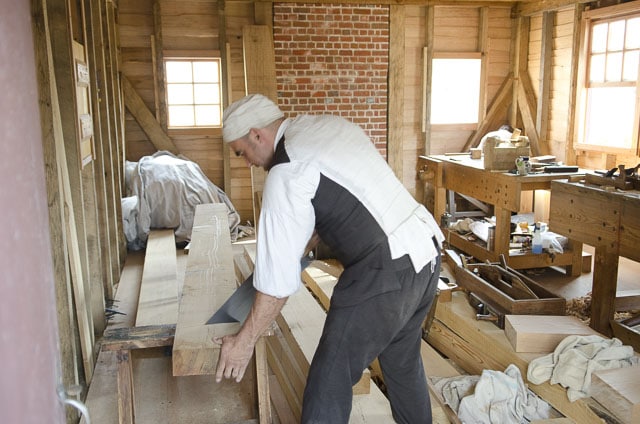 A Traditional Woodworker Uses A Hand Saw To Cut A Thick Board On A Saw Bench In A Colonial Williamsburg Woodworking Workshop