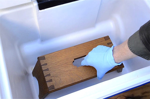 A Gloved Hand Setting An Oak Moravian Footstool Inside A Cooler For Ammonia Fuming