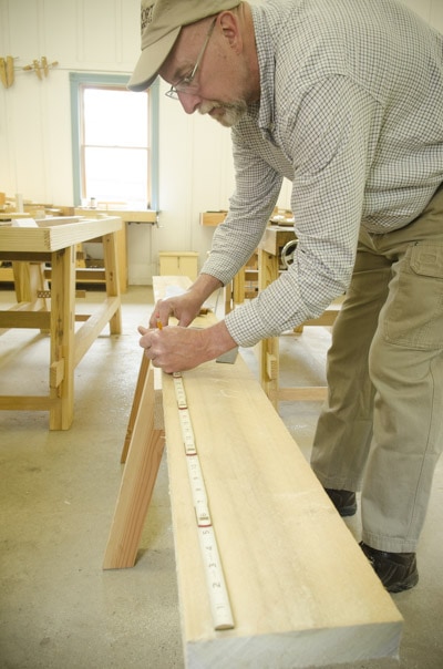 An Older Woodworking Student Using An Antique Zig Zag Rule Ruler To Measure A Board On A Saw Horse