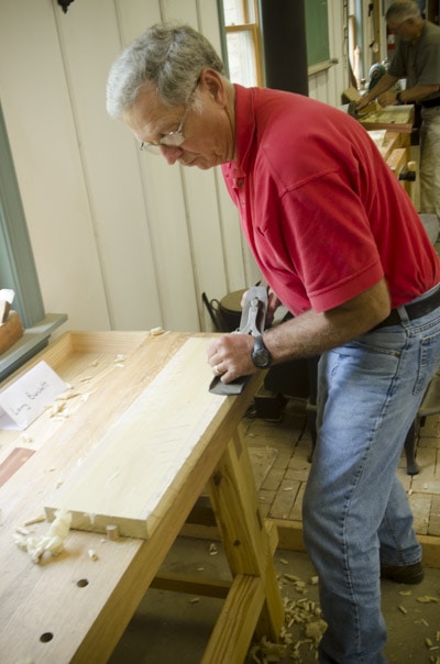 An Older Male Woodworking Student Using An Antique Stanley 7 Jointer Plane To Flatten A Board At A Woodworking Workbench