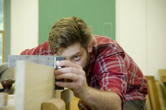 An Bearded Woodworking Student Checking A Board With A Try Square At A Woodworking Workbench