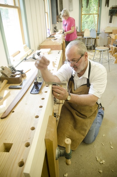An Older Male Woodworking Student Checking A Board With A Try Square At A Woodworking Workbench