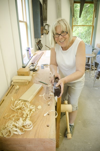 An Older Female Woodworking Student Using A Come And Go Tongue And Groove Plane At A Roubo Workbench