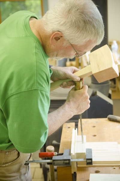 An Older Woodworker Chopping A Mortise And Tenon Joint With A Joiner'S Mallet And Mortise Chisel