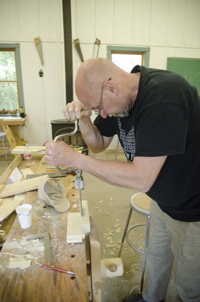 An Older Male Woodworking Student Using An Antique Brace And Bit To Bore A Hole In A Tenon And Mortise Joint
