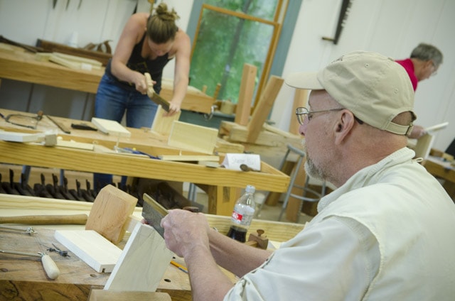 An Older Woodworking Student Using A Dovetail Saw To Cut Dovetail Joints With A Female Woodworker Cutting Dovetails In The Background