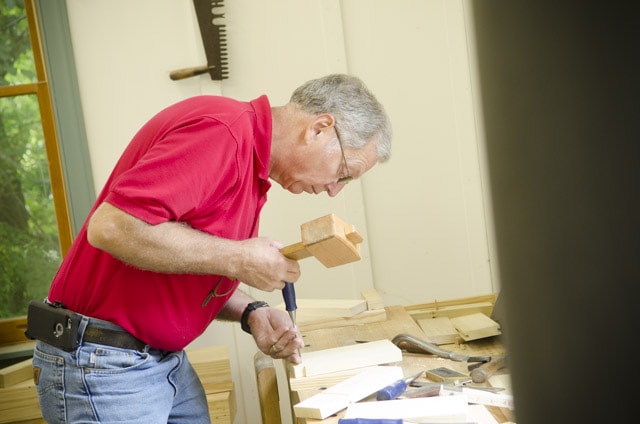 An Older Woodworker Chopping A Mortise And Tenon Joint With A Joiner'S Mallet And Mortise Chisel
