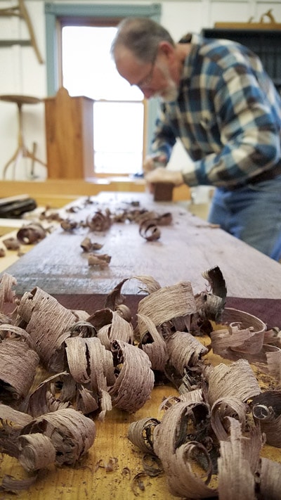 Older Man Using A Hand Plane To Flatten A Board With Shavings In The Foreground