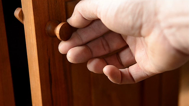 Hand Twisting A Cherry Shaker Knob On A Frame And Panel Door Of A Cupboard