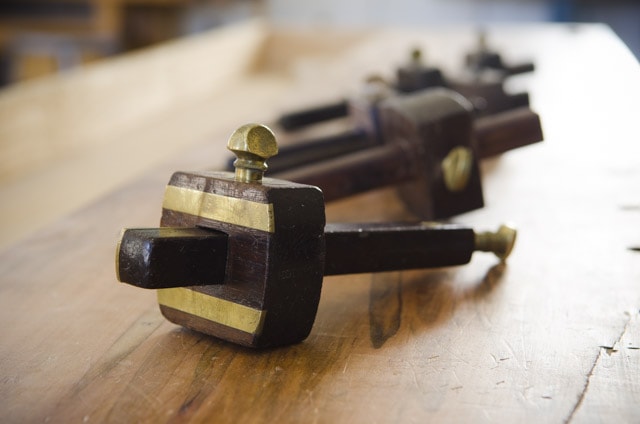 A Row Of Antique Mortise Gauges And Marking Gauges On A Woodworking Workbench