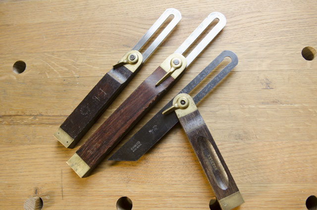 Three Sliding T Bevel Squares With Locking Levers Laying On A Woodworking Workbench