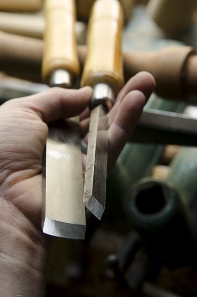 Two Woodturning Skew Chisels In A Hand In Front Of A Wood Turning Lathe