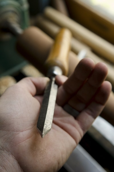 Wood Turning Parting Tool Chisel In A Hand In Front Of A Wood Lathe