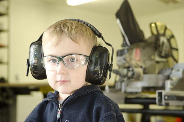 Young Boy Wearing Safety Glasses And Hearing Protection In A Woodworking Workshop