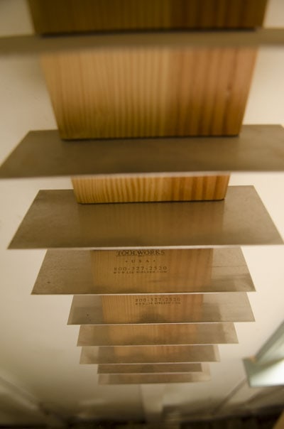A Vertical Row Of Card Scrapers Sitting In Slots On A Wooden Shelf For Woodworking