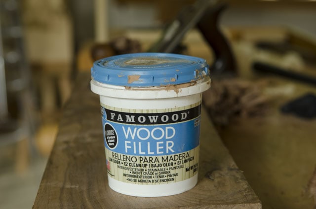 Plastic Container Of Famowood Red Oak Wood Filler With A Handplane In The Background Sitting On A Woodworking Workbench