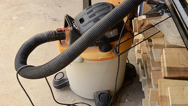 Shop Vac Vacuum Hooked Up To A Router Table With Lumber In The Backgorund