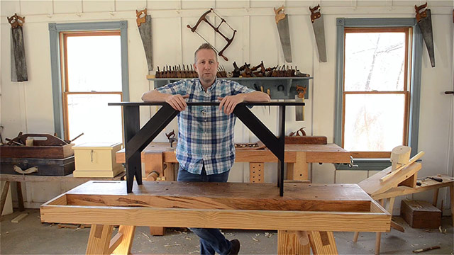 Joshua Farnsworth Standing In His Woodworking Workshop Over A Shaker Bench