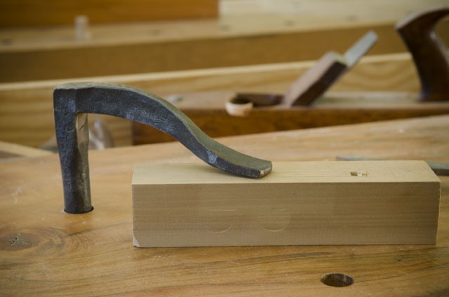 Blacksmith Forged Holdfast Holding Down A Piece Of Wood On A Woodworking Bench Workbench With A Handplane In The Background