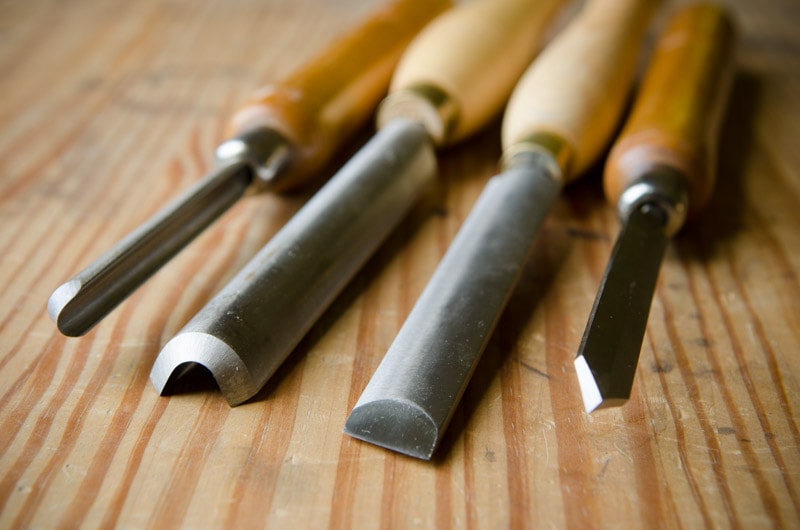 Four Wood Turning Chisels On A Wooden Workbench Including A Skew Chisel, A Detail Spindle Gouge, A Rouging Gouge, And A Diamond Parting Tool